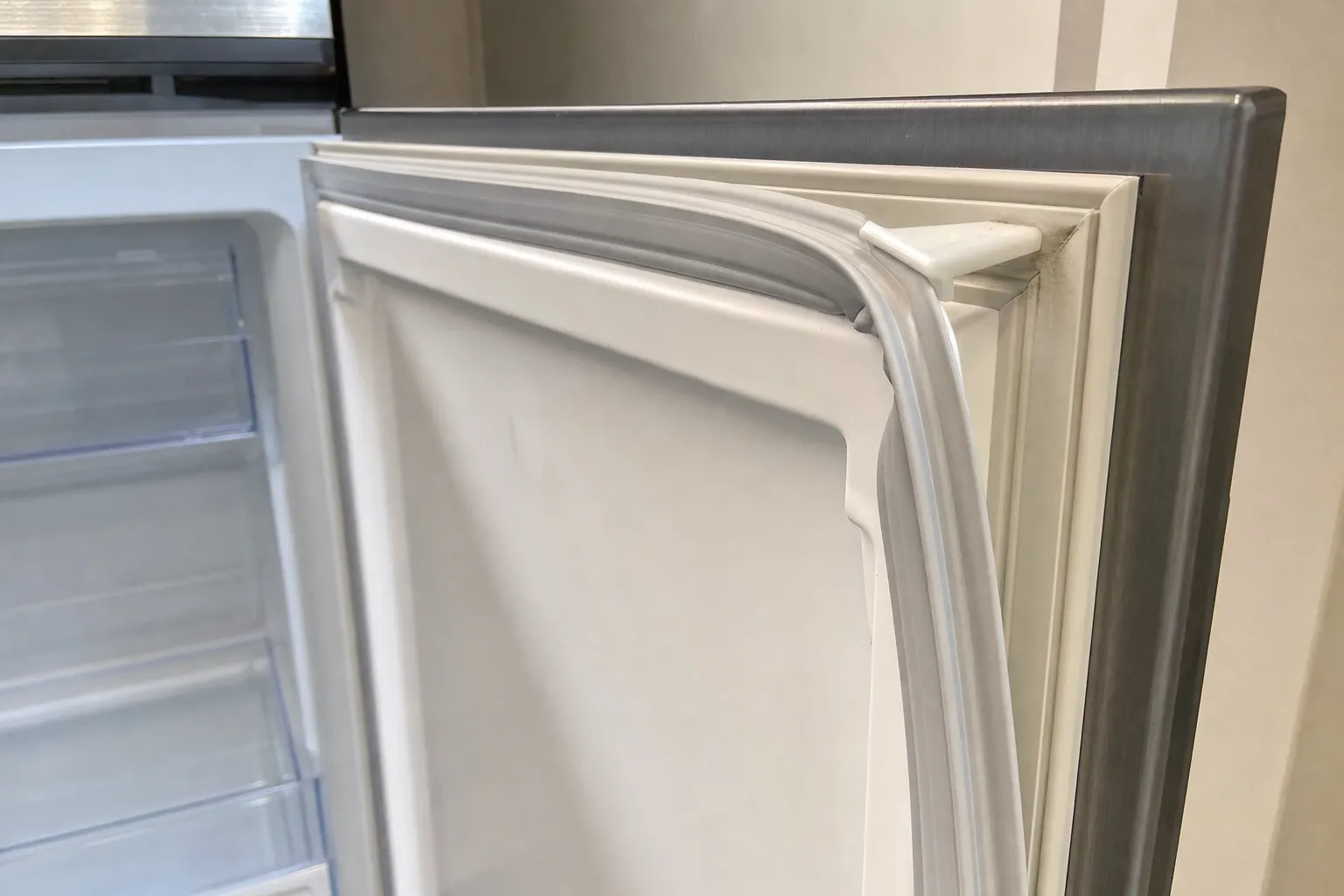 Close-up of the magnetic gasket along the edge of an open stainless-fronted door, chilled compartment behind